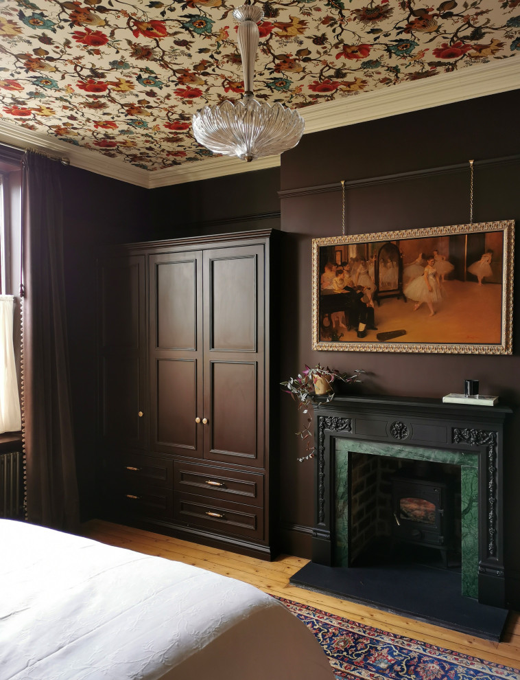 Großes Klassisches Hauptschlafzimmer mit lila Wandfarbe, braunem Holzboden, Kaminofen, Kaminumrandung aus Stein, beigem Boden und Tapetendecke in Sonstige
