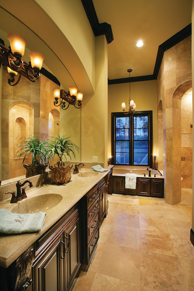 This is an example of a large mediterranean master bathroom in Miami with an integrated sink, raised-panel cabinets, dark wood cabinets, a drop-in tub, a corner shower, beige tile, stone tile, beige walls and travertine floors.