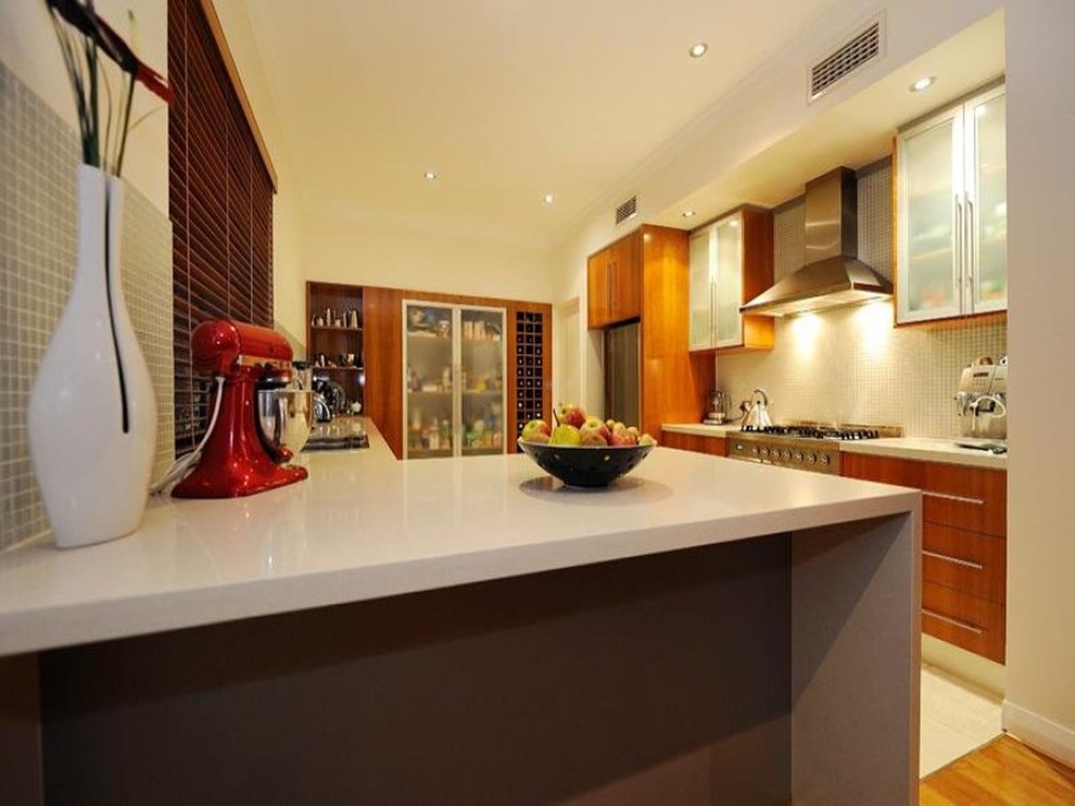 This is an example of a small contemporary l-shaped eat-in kitchen in Perth with an undermount sink, glass-front cabinets, light wood cabinets, quartz benchtops, white splashback, mosaic tile splashback, stainless steel appliances and porcelain floors.