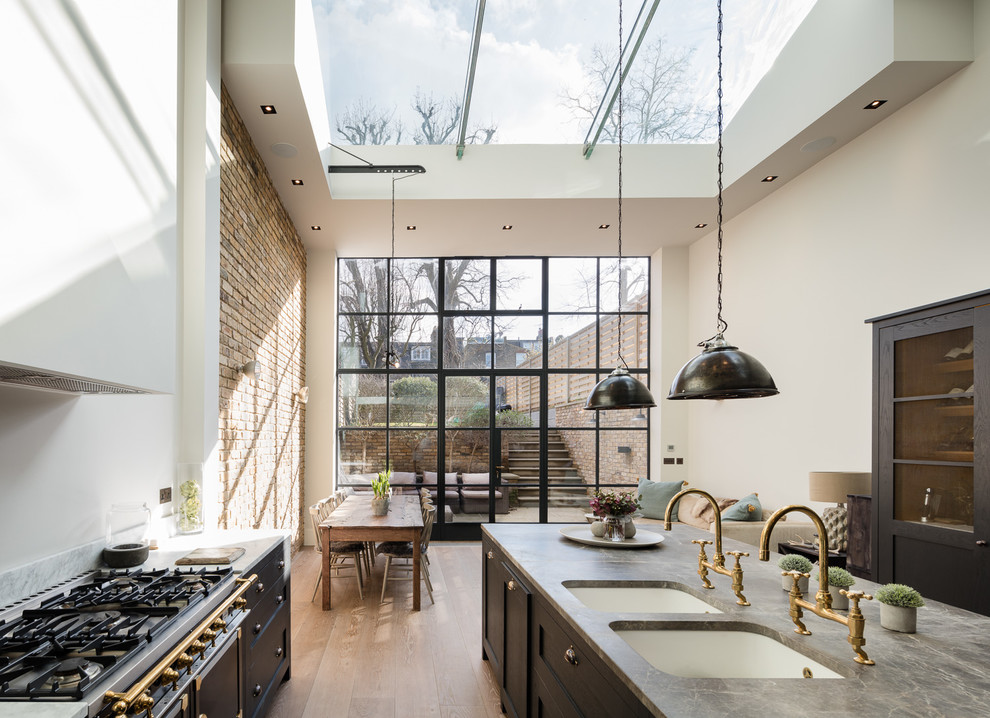 This is an example of a large industrial galley open plan kitchen in London with a double-bowl sink, shaker cabinets, grey cabinets, marble benchtops, black appliances, medium hardwood floors and with island.