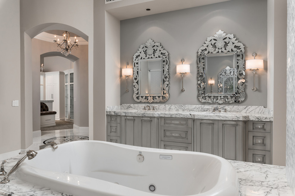 Photo of an expansive mediterranean master bathroom in Phoenix with raised-panel cabinets, grey cabinets, a drop-in tub, an open shower, a one-piece toilet, multi-coloured tile, marble, beige walls, marble floors, an integrated sink, marble benchtops, multi-coloured floor, an open shower, multi-coloured benchtops, a niche, a double vanity, a built-in vanity, coffered and panelled walls.