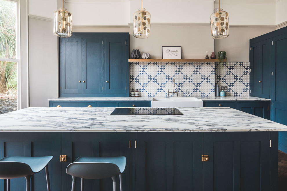Design ideas for a large transitional l-shaped eat-in kitchen in Other with a farmhouse sink, shaker cabinets, blue cabinets, marble benchtops, cement tile splashback, dark hardwood floors, with island, brown floor, multi-coloured splashback and panelled appliances.