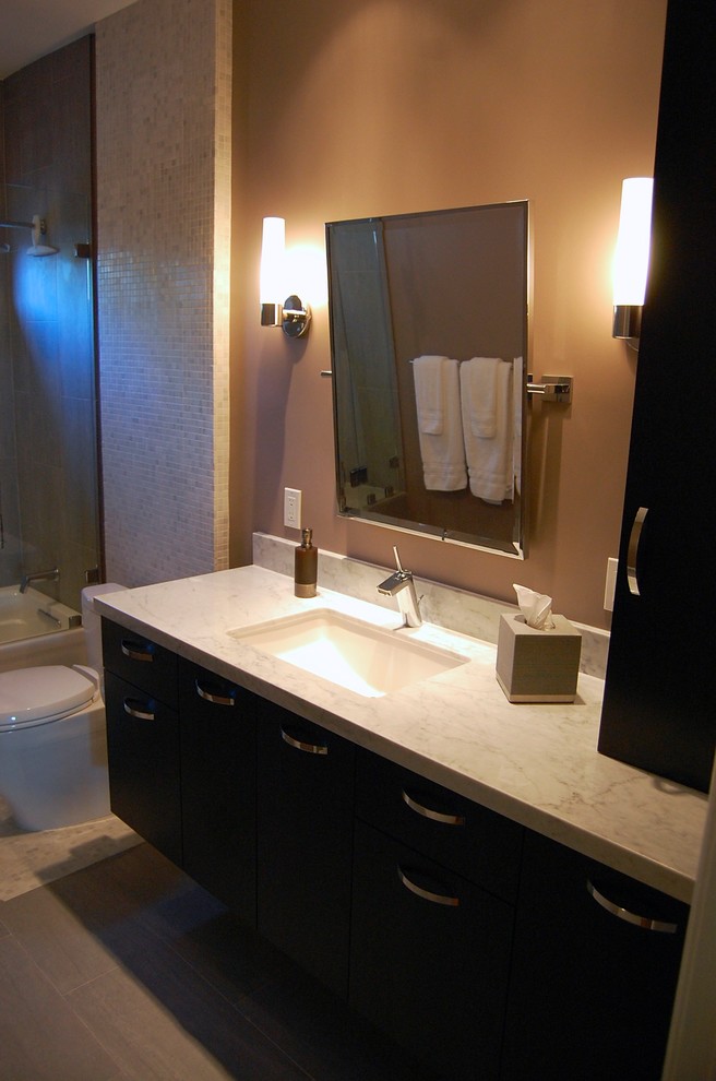 This is an example of a mid-sized contemporary master bathroom in Los Angeles with flat-panel cabinets, dark wood cabinets, a shower/bathtub combo, a one-piece toilet, beige tile, mosaic tile, brown walls, travertine floors, an undermount sink and quartzite benchtops.