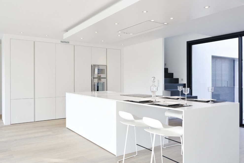 Photo of a large contemporary single-wall eat-in kitchen in Le Havre with white cabinets, stainless steel appliances, light hardwood floors and with island.