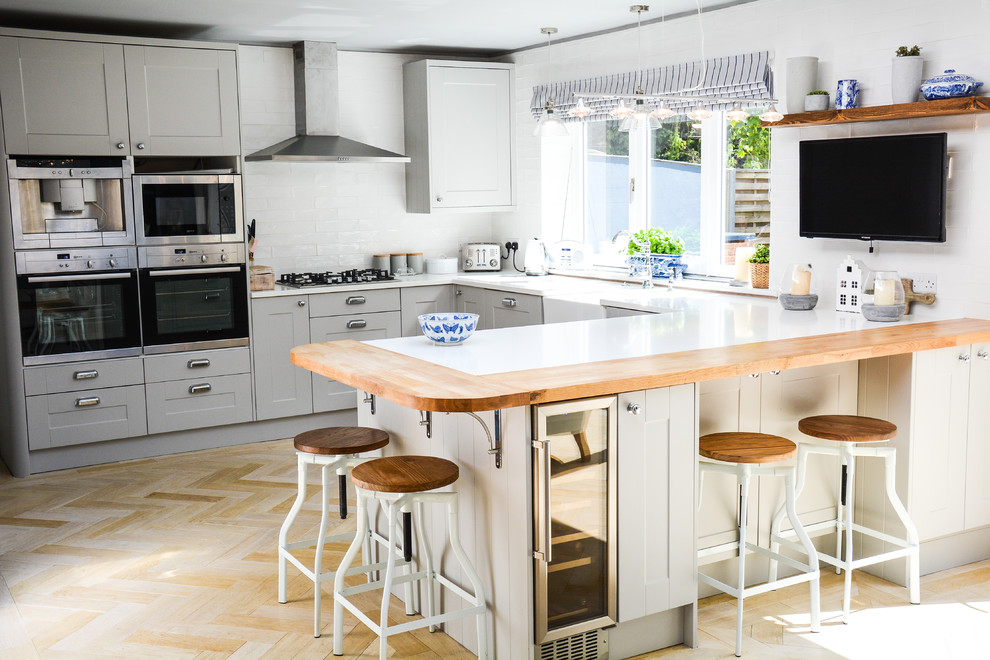 Design ideas for a transitional u-shaped kitchen in Hampshire with shaker cabinets, grey cabinets, white splashback, subway tile splashback, light hardwood floors and beige floor.