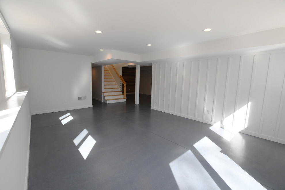 This is an example of a large midcentury walk-out basement in New York with white walls, concrete floors, grey floor and panelled walls.