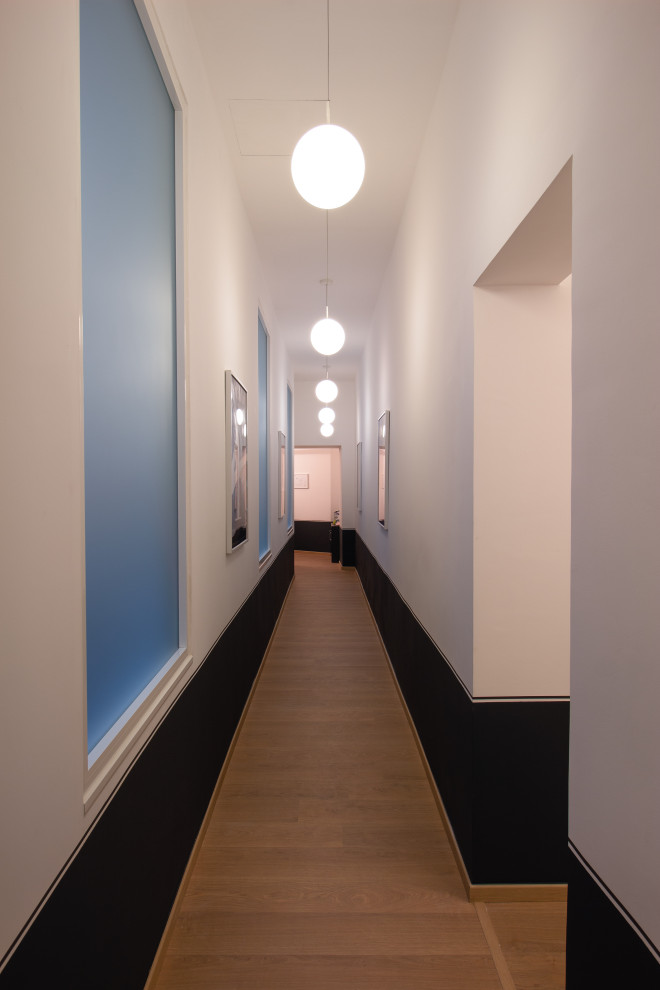 На фото: большой коридор в современном стиле с белыми стенами, светлым паркетным полом и панелями на стенах с
