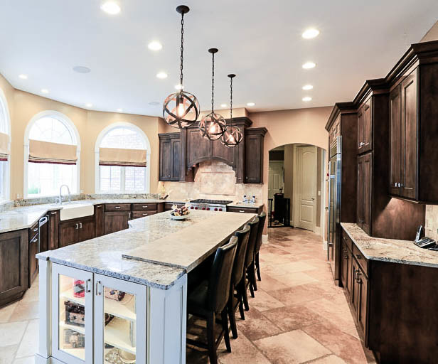 Inspiration for a large rustic u-shaped travertine floor eat-in kitchen remodel in Cleveland with a farmhouse sink, recessed-panel cabinets, dark wood cabinets, granite countertops, stone tile backsplash, stainless steel appliances, an island, beige backsplash and beige countertops