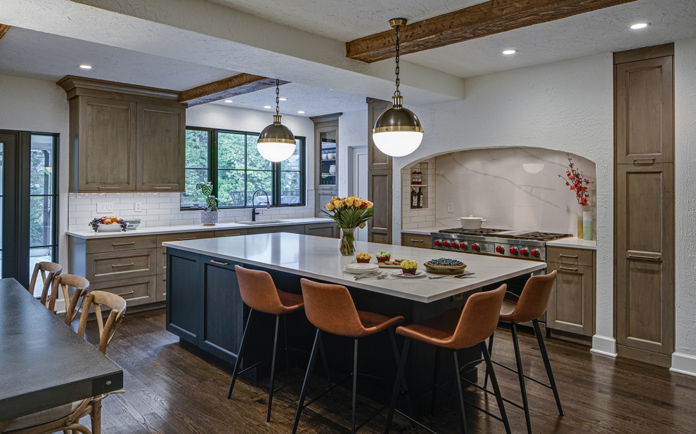 This is an example of a transitional l-shaped open plan kitchen in Chicago with grey cabinets, quartz benchtops, white splashback, engineered quartz splashback, stainless steel appliances, with island, brown floor and white benchtop.