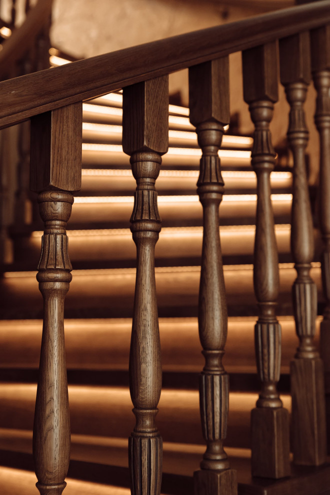 Ejemplo de escalera curva clásica grande con escalones de madera, contrahuellas de madera, barandilla de madera y papel pintado