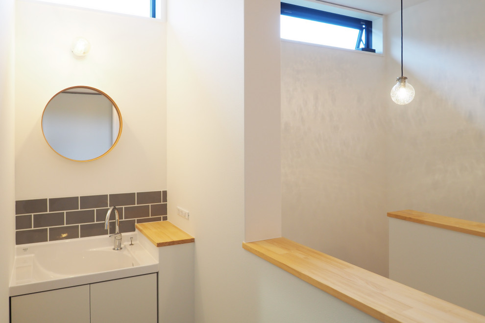 На фото: туалет в стиле модернизм с белыми фасадами, серой плиткой, плиткой кабанчик, белой столешницей, встроенной тумбой, потолком с обоями и обоями на стенах