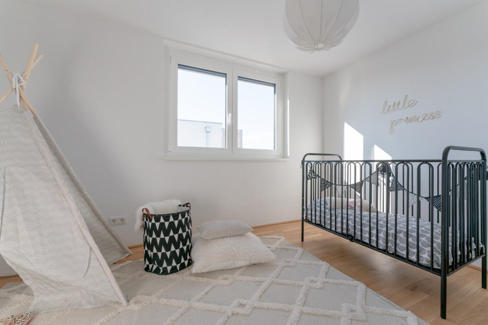 Cette photo montre une très grande chambre de bébé neutre moderne avec un mur blanc et parquet clair.