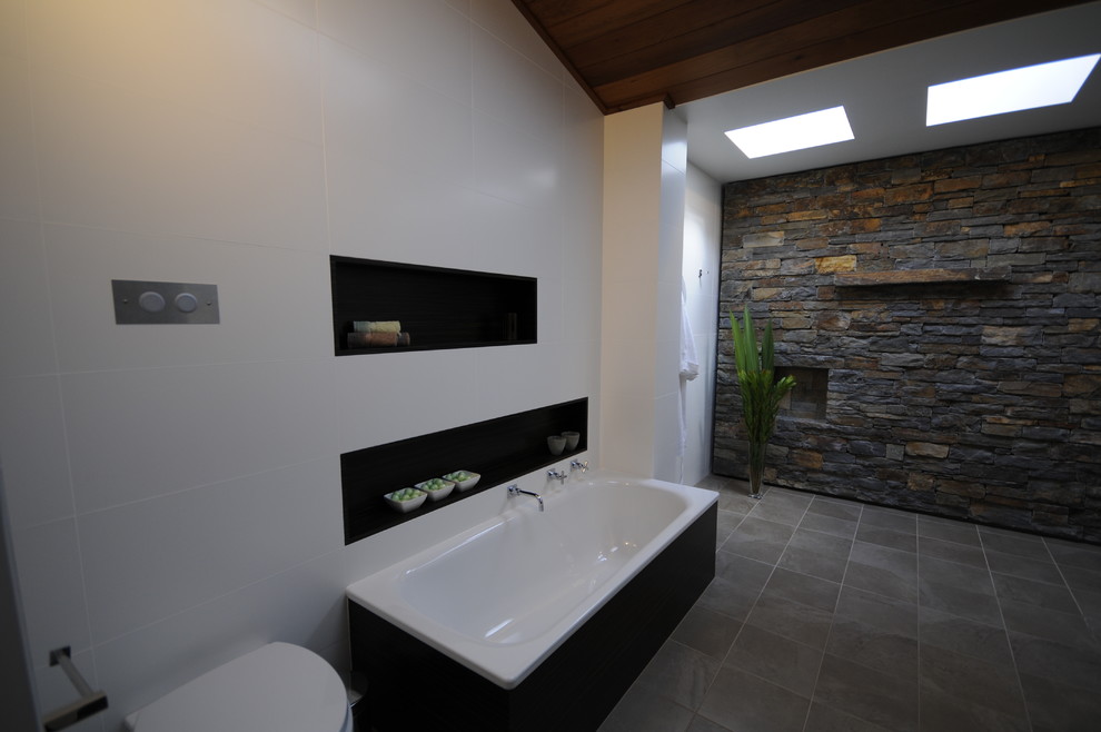 Inspiration for a modern master bathroom in Wollongong with a vessel sink, flat-panel cabinets, dark wood cabinets, solid surface benchtops, a drop-in tub, an open shower, a wall-mount toilet, white tile, ceramic tile, white walls and ceramic floors.