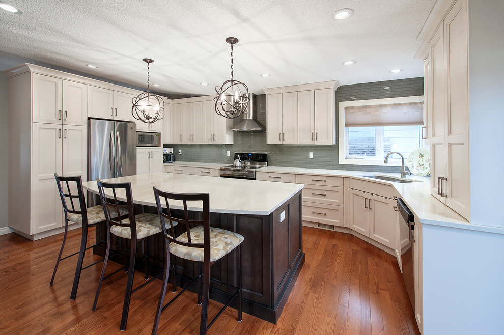 Example of a large transitional l-shaped dark wood floor eat-in kitchen design in Calgary with an undermount sink, recessed-panel cabinets, white cabinets, solid surface countertops, green backsplash, glass tile backsplash, stainless steel appliances and an island