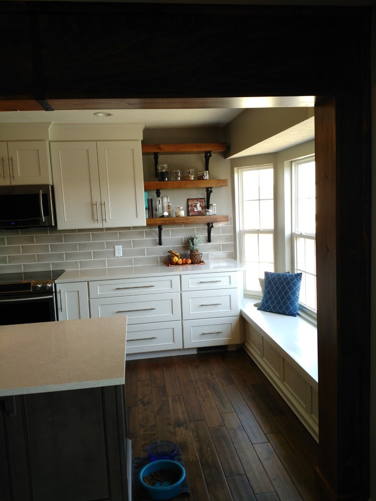 Mid-sized transitional l-shaped dark wood floor and brown floor eat-in kitchen photo with a single-bowl sink, shaker cabinets, white cabinets, quartzite countertops, gray backsplash, ceramic backsplash, stainless steel appliances and an island