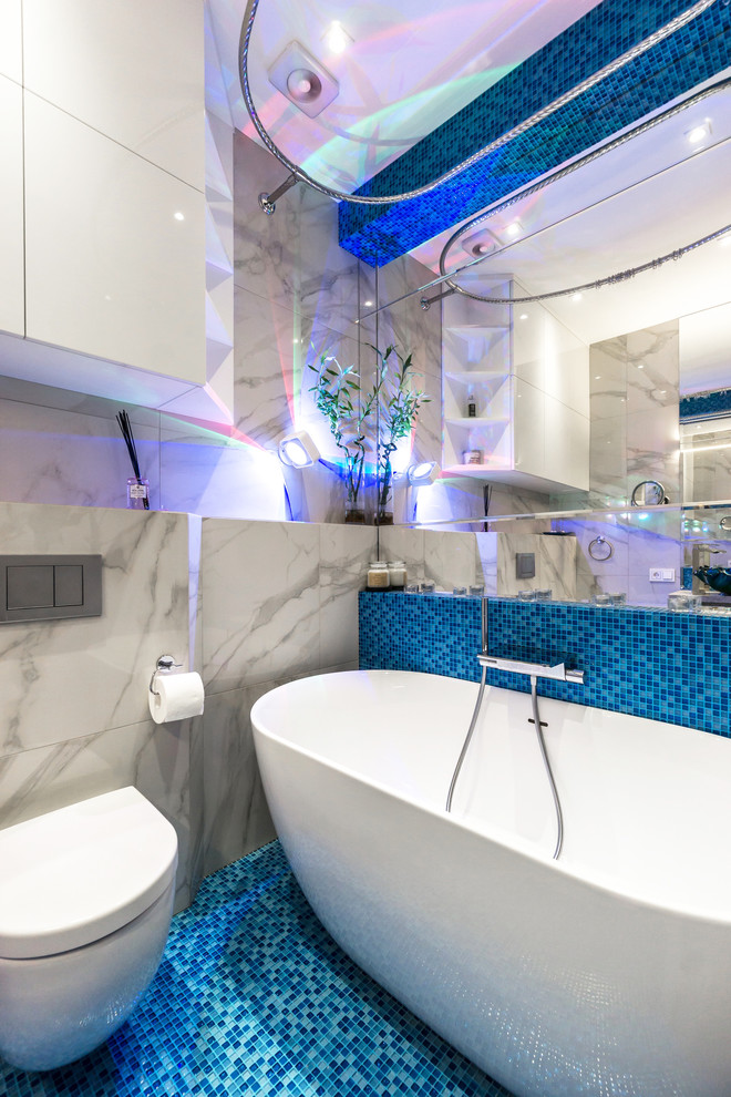Small contemporary kids bathroom in Moscow with a wall-mount toilet, blue tile, mosaic tile, flat-panel cabinets, white cabinets, a freestanding tub, blue walls, mosaic tile floors, a drop-in sink, solid surface benchtops, blue floor and white benchtops.