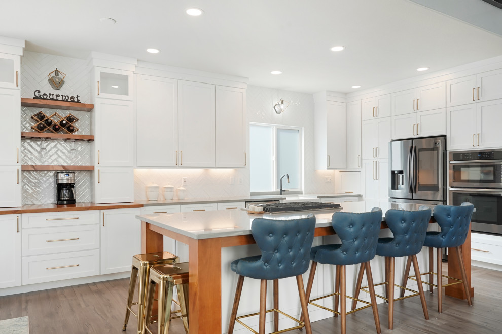 Open concept kitchen - large transitional l-shaped open concept kitchen idea in Denver with a farmhouse sink, shaker cabinets, white cabinets, quartz countertops, white backsplash, ceramic backsplash, stainless steel appliances, an island and gray countertops