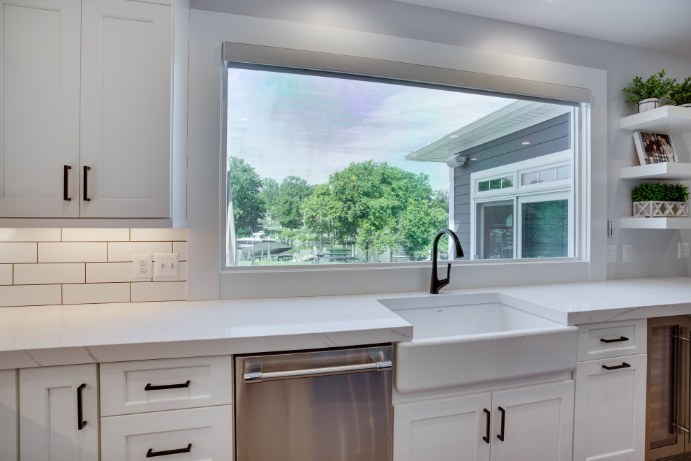 Design ideas for a large beach style l-shaped eat-in kitchen in Baltimore with a farmhouse sink, quartz benchtops, white splashback, subway tile splashback, stainless steel appliances, with island and white benchtop.