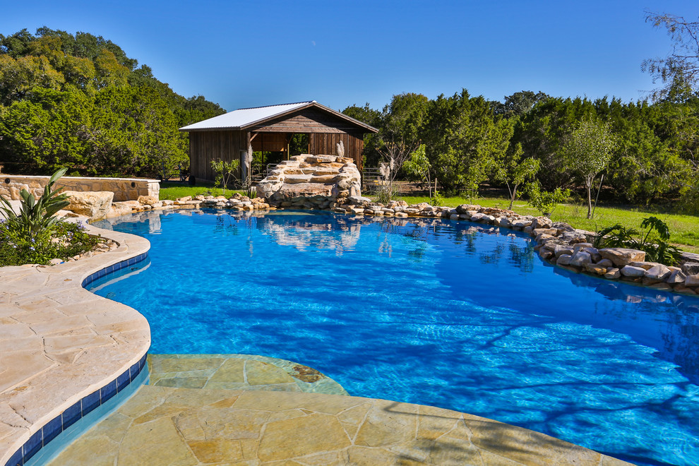 This is an example of a large country backyard custom-shaped pool in Austin with natural stone pavers.