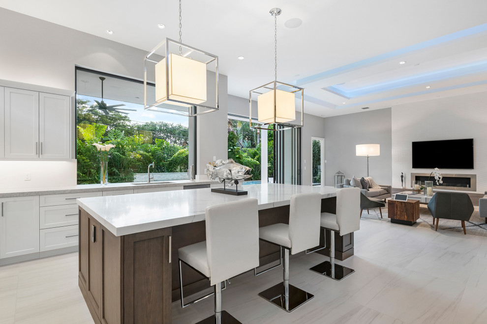 This is an example of a large contemporary l-shaped open plan kitchen in Miami with flat-panel cabinets, light wood cabinets, porcelain floors, white floor, an undermount sink, quartz benchtops, white splashback, engineered quartz splashback, stainless steel appliances, with island, white benchtop and coffered.