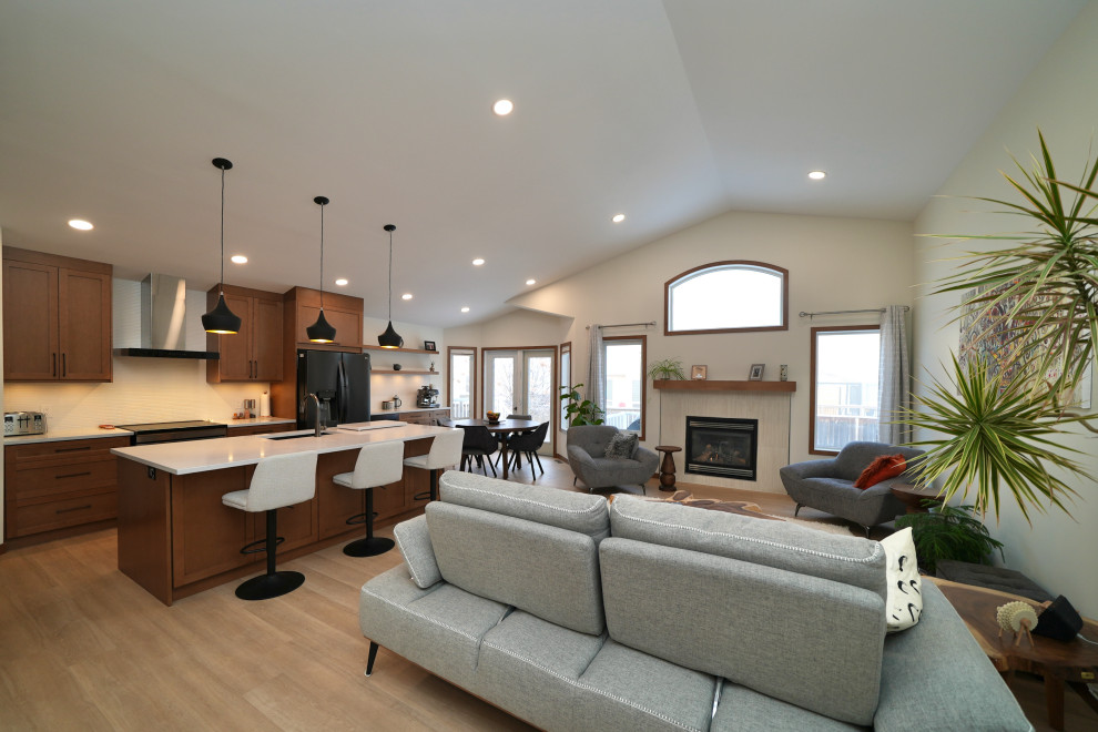 Example of a l-shaped vinyl floor and beige floor eat-in kitchen design with a single-bowl sink, shaker cabinets, brown cabinets, quartz countertops, white backsplash, ceramic backsplash, black appliances, an island and white countertops