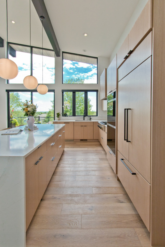 This is an example of a midcentury l-shaped open plan kitchen in Other with an undermount sink, flat-panel cabinets, light wood cabinets, quartz benchtops, engineered quartz splashback, stainless steel appliances, light hardwood floors, with island, brown floor, white benchtop and vaulted.