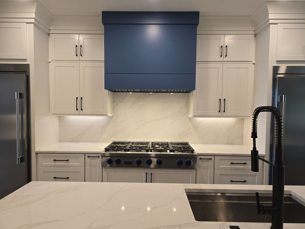 Kitchen - large modern l-shaped kitchen idea with an undermount sink, shaker cabinets, white cabinets, quartz countertops, white backsplash, quartz backsplash, stainless steel appliances, an island and white countertops