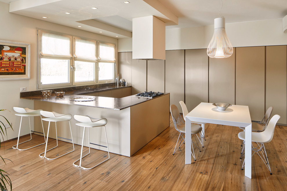 Contemporary u-shaped eat-in kitchen with flat-panel cabinets, beige cabinets, an undermount sink, medium hardwood floors, a peninsula, brown floor, marble benchtops, black splashback, marble splashback, stainless steel appliances and black benchtop.