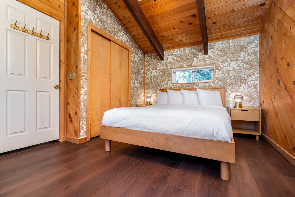 Cette image montre une chambre parentale bohème de taille moyenne avec un mur marron, un sol en vinyl, un poêle à bois, un manteau de cheminée en brique, un sol marron et poutres apparentes.