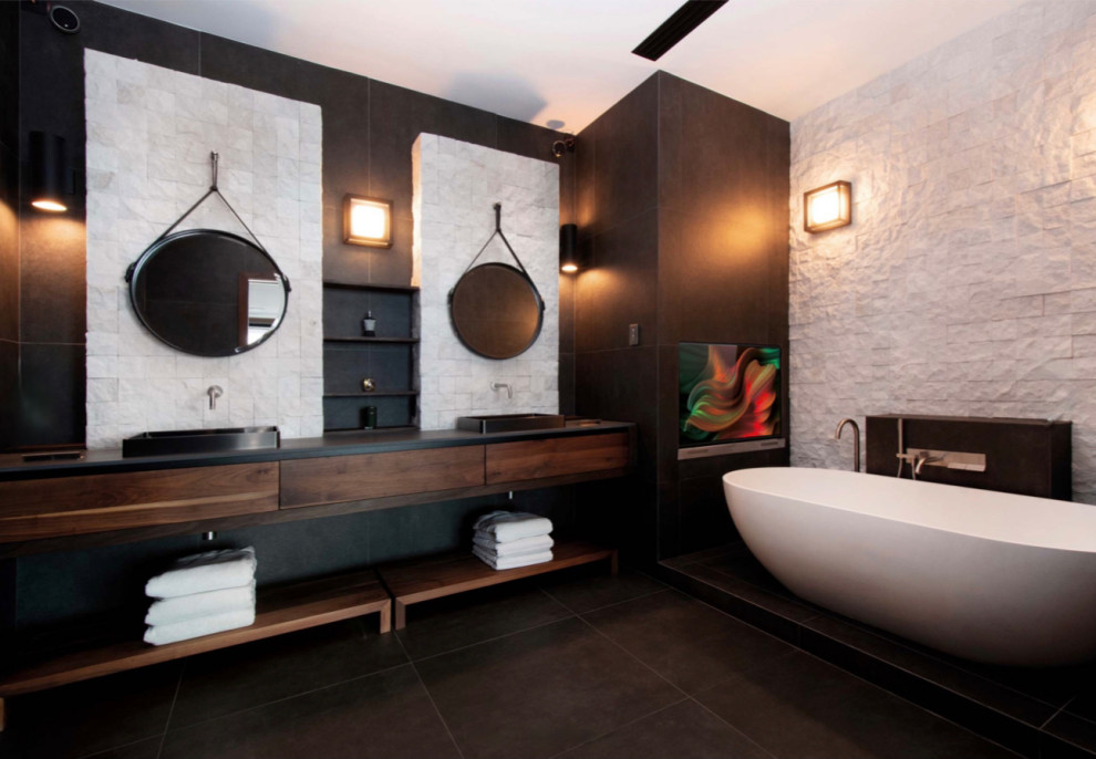 На фото: большая главная ванная комната в стиле модернизм с плоскими фасадами, темными деревянными фасадами, отдельно стоящей ванной, двойным душем, инсталляцией, черно-белой плиткой, керамогранитной плиткой, черными стенами, полом из керамогранита, настольной раковиной, столешницей из гранита, черным полом, душем с распашными дверями, серой столешницей, сиденьем для душа, тумбой под две раковины и подвесной тумбой