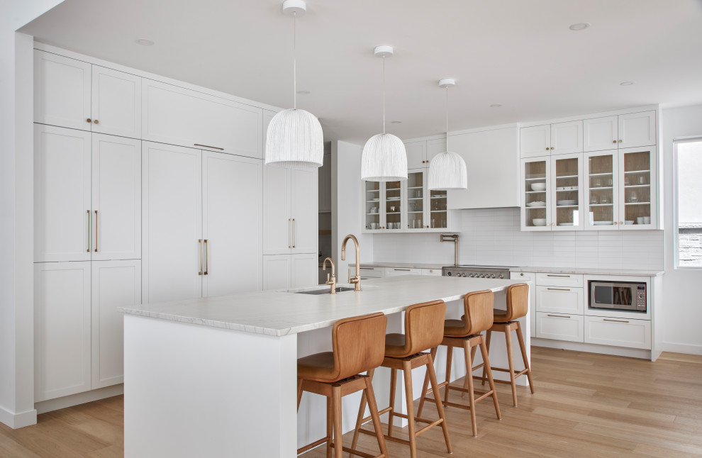 Eat-in kitchen - transitional l-shaped light wood floor eat-in kitchen idea in Ottawa with shaker cabinets, white cabinets, quartzite countertops, white backsplash, ceramic backsplash, paneled appliances and an island