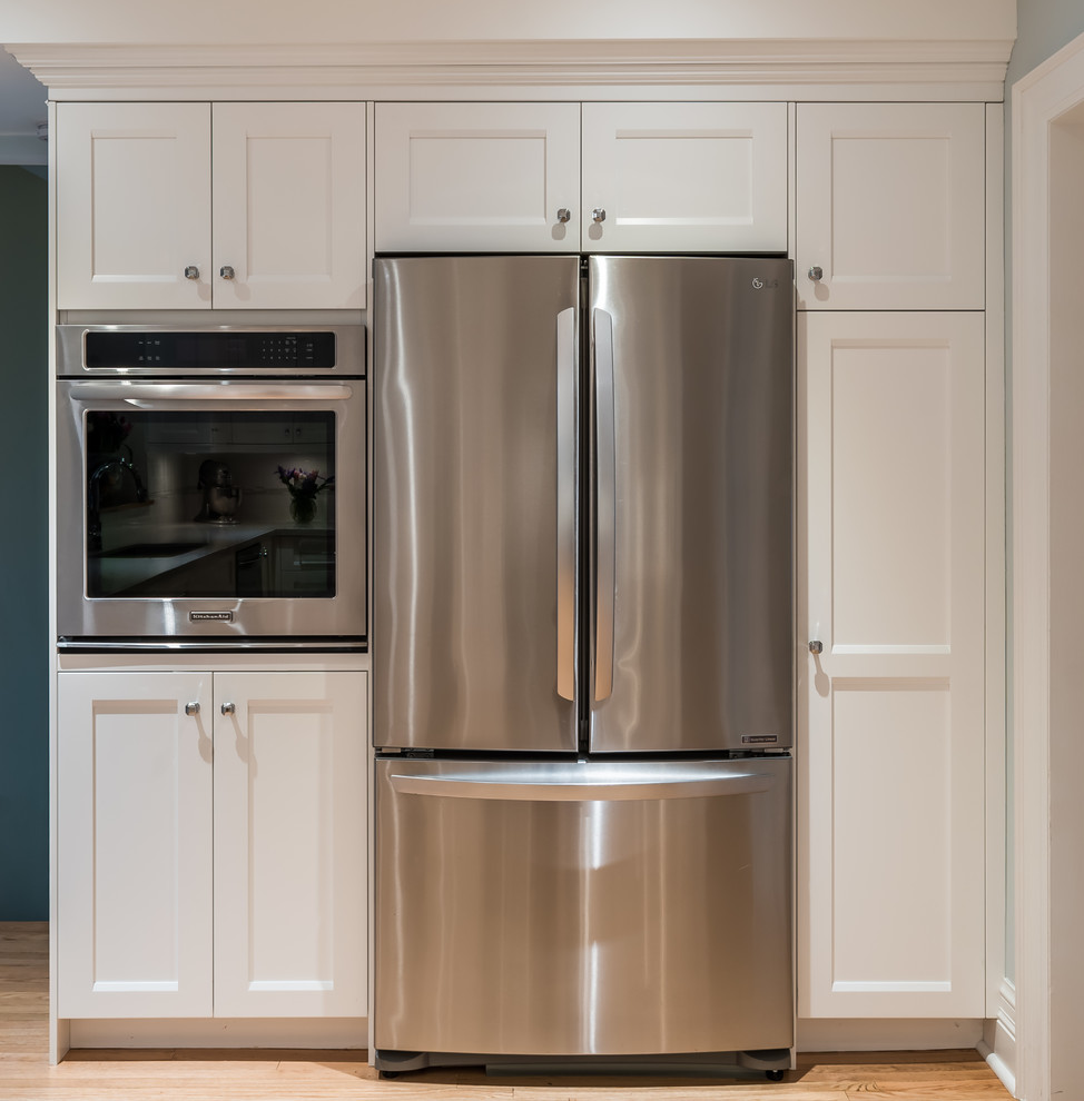 Example of a large transitional u-shaped light wood floor enclosed kitchen design in Toronto with an undermount sink, shaker cabinets, white cabinets, quartz countertops, white backsplash, stone tile backsplash, stainless steel appliances and no island