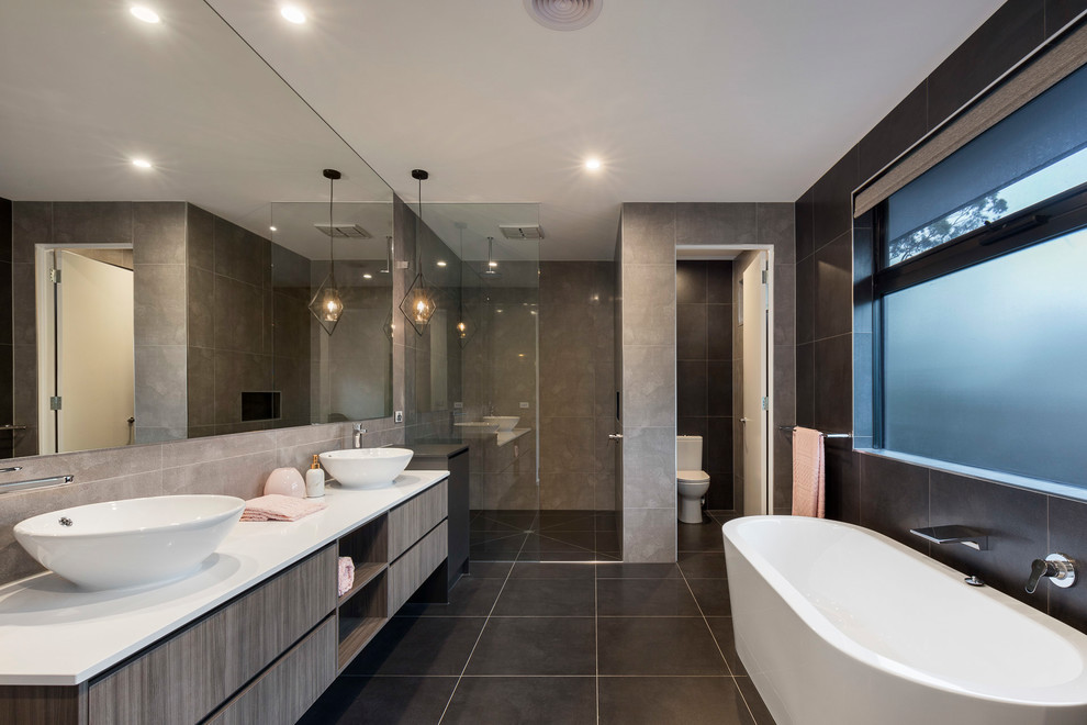 Contemporary master bathroom in Melbourne with flat-panel cabinets, dark wood cabinets, a freestanding tub, a corner shower, gray tile, black walls, a vessel sink, black floor and white benchtops.