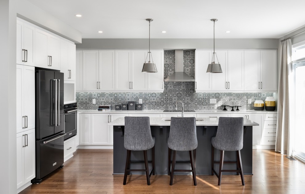 Inspiration for a large transitional l-shaped eat-in kitchen in Ottawa with an undermount sink, recessed-panel cabinets, white cabinets, quartz benchtops, porcelain splashback, medium hardwood floors, with island, brown floor, grey splashback and black appliances.