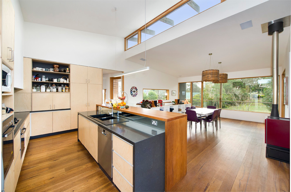 Photo of a mid-sized contemporary u-shaped eat-in kitchen in Melbourne with a drop-in sink, flat-panel cabinets, light wood cabinets, stainless steel appliances, medium hardwood floors, with island, brown floor and black benchtop.