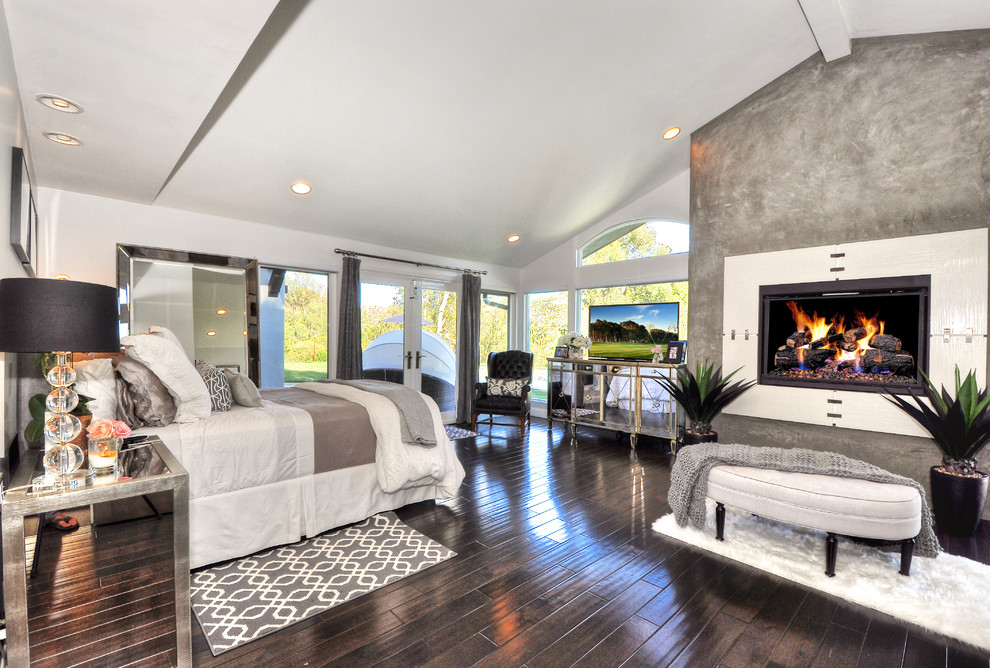 Photo of a large transitional master bedroom in Orange County with white walls, dark hardwood floors, a standard fireplace, a concrete fireplace surround and brown floor.