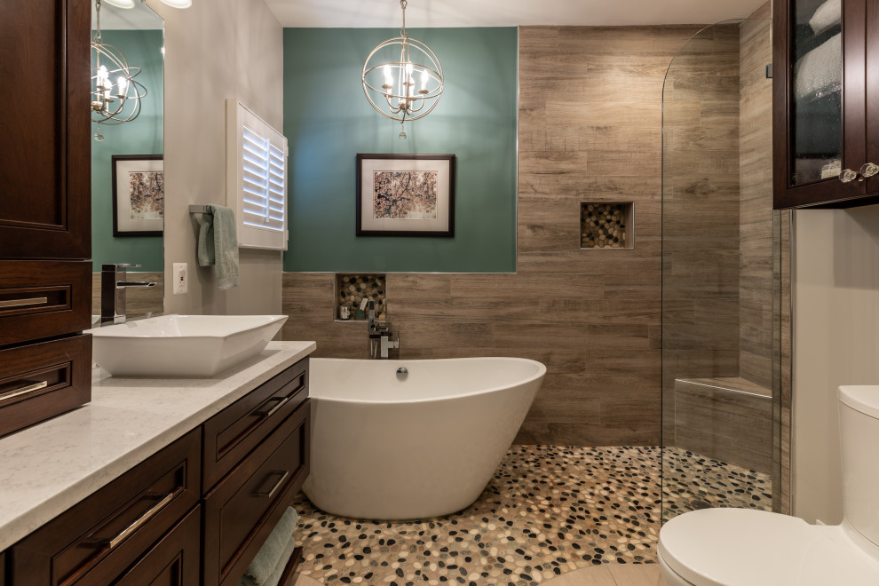This is an example of a large traditional ensuite bathroom in DC Metro with recessed-panel cabinets, dark wood cabinets, a freestanding bath, a walk-in shower, a two-piece toilet, brown tiles, wood-effect tiles, beige walls, a vessel sink, marble worktops, beige floors, an open shower, white worktops, double sinks and a built in vanity unit.