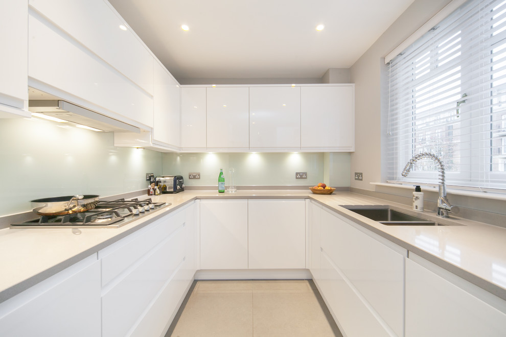 This is an example of a small contemporary u-shaped separate kitchen in Other with a double-bowl sink, flat-panel cabinets, white cabinets, quartz benchtops, glass sheet splashback, ceramic floors, no island, green splashback, stainless steel appliances, beige floor and grey benchtop.