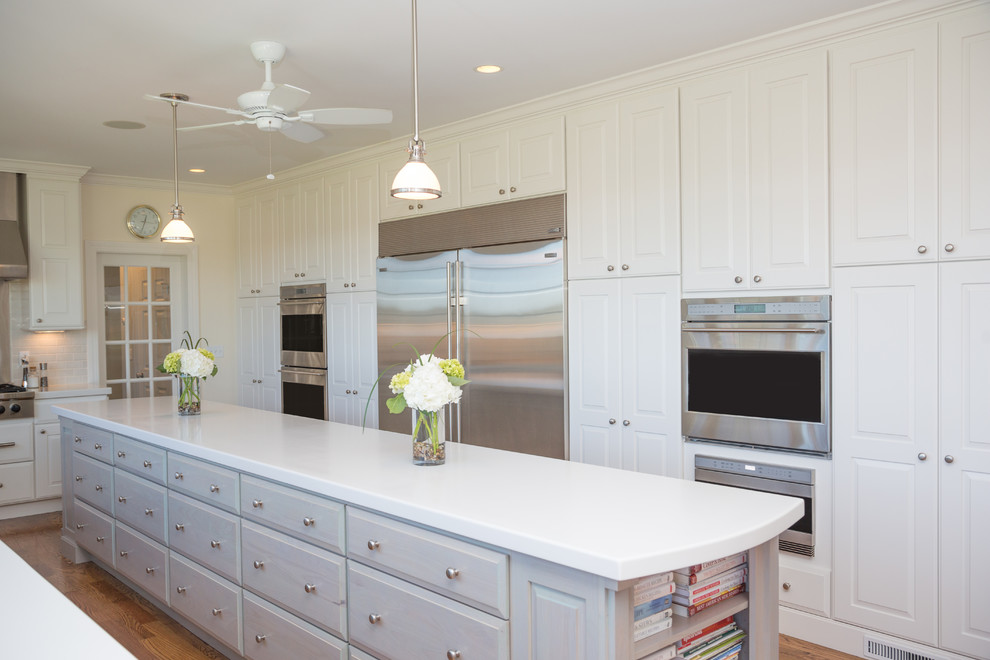 This is an example of a traditional eat-in kitchen in New York with white cabinets, marble benchtops, white splashback, ceramic splashback, stainless steel appliances, medium hardwood floors and with island.