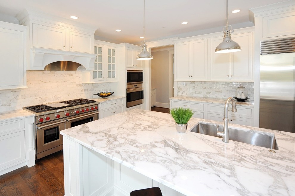 Eat-in kitchen - large l-shaped medium tone wood floor eat-in kitchen idea in DC Metro with a drop-in sink, recessed-panel cabinets, white cabinets, marble countertops, white backsplash, stone slab backsplash, stainless steel appliances and an island