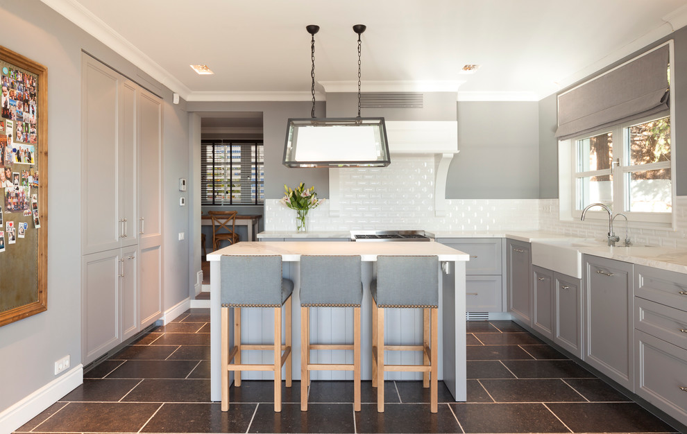 This is an example of a mid-sized transitional l-shaped eat-in kitchen in Barcelona with a farmhouse sink, shaker cabinets, grey cabinets, white splashback, subway tile splashback, stainless steel appliances and with island.