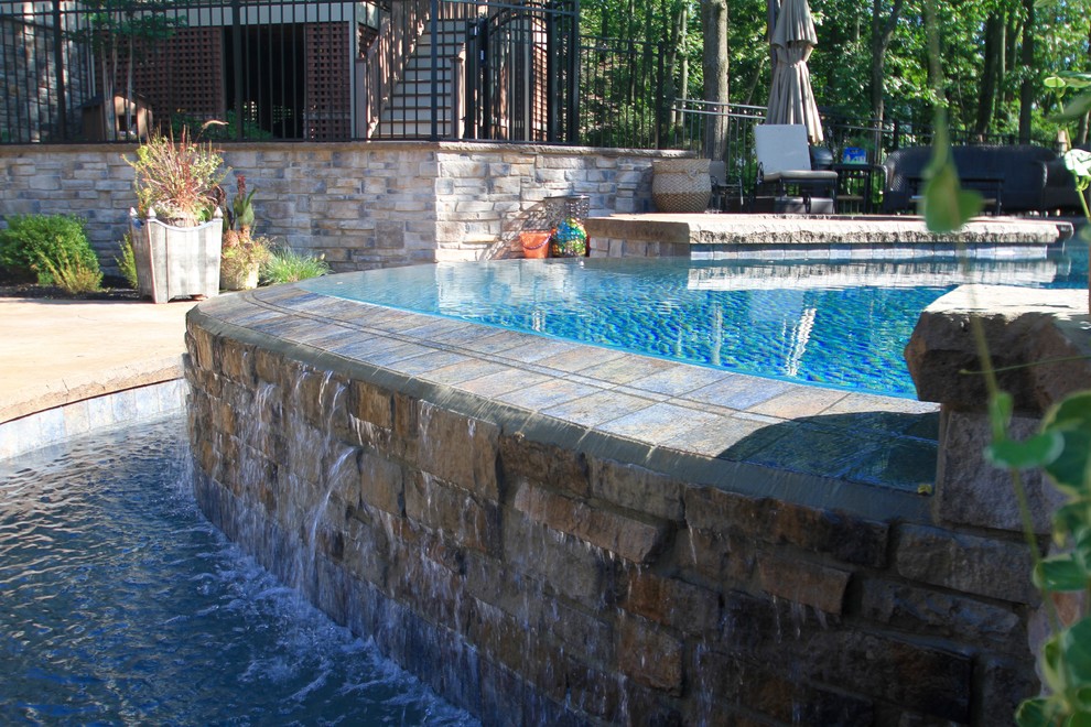 Design ideas for a large contemporary backyard custom-shaped infinity pool in Philadelphia with a hot tub and stamped concrete.