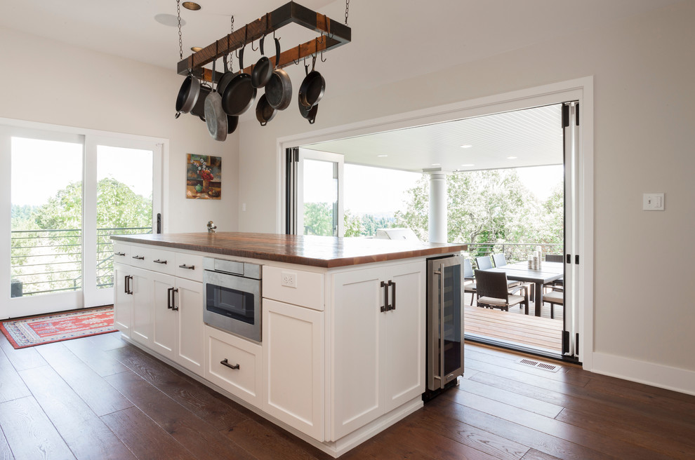 Large transitional l-shaped eat-in kitchen in Portland with shaker cabinets, white cabinets, wood benchtops, white splashback, stainless steel appliances, plywood floors, with island, brown floor and brown benchtop.