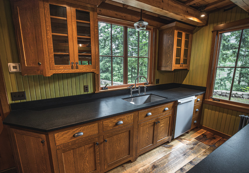 Example of a mountain style medium tone wood floor and exposed beam kitchen design with an undermount sink, shaker cabinets, granite countertops, black backsplash, granite backsplash, stainless steel appliances, an island and black countertops