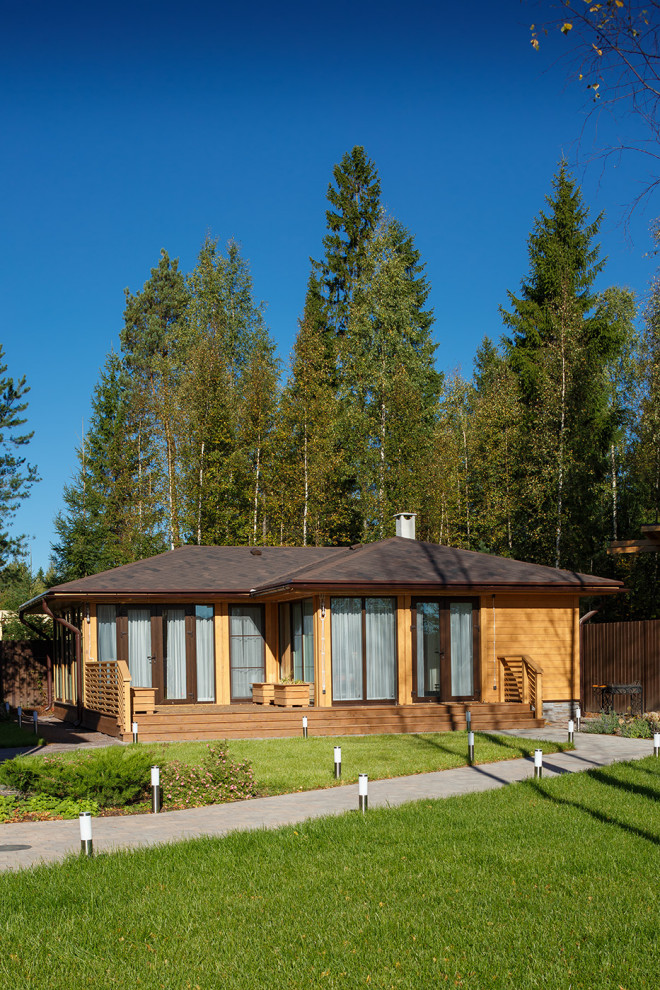 На фото: одноэтажный, деревянный, оранжевый частный загородный дом среднего размера в современном стиле с вальмовой крышей, крышей из гибкой черепицы и коричневой крышей
