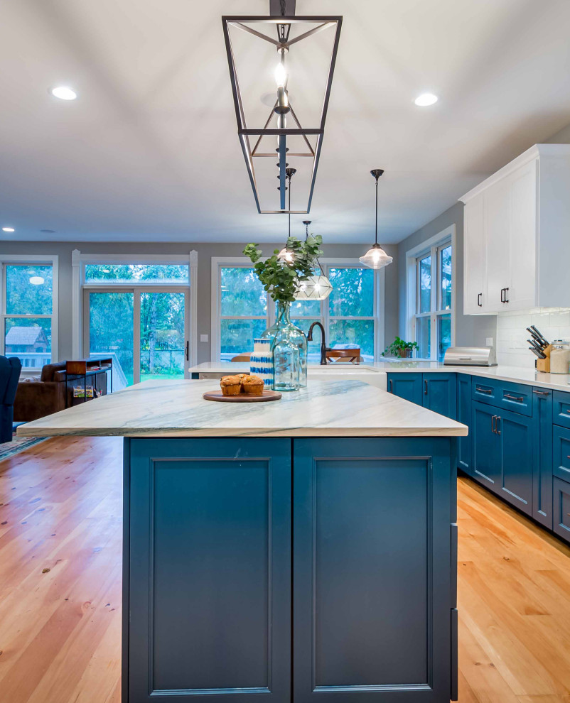 Photo of a large country l-shaped eat-in kitchen in Chicago with a farmhouse sink, shaker cabinets, turquoise cabinets, marble benchtops, white splashback, porcelain splashback, stainless steel appliances, light hardwood floors, with island, brown floor, multi-coloured benchtop and wallpaper.