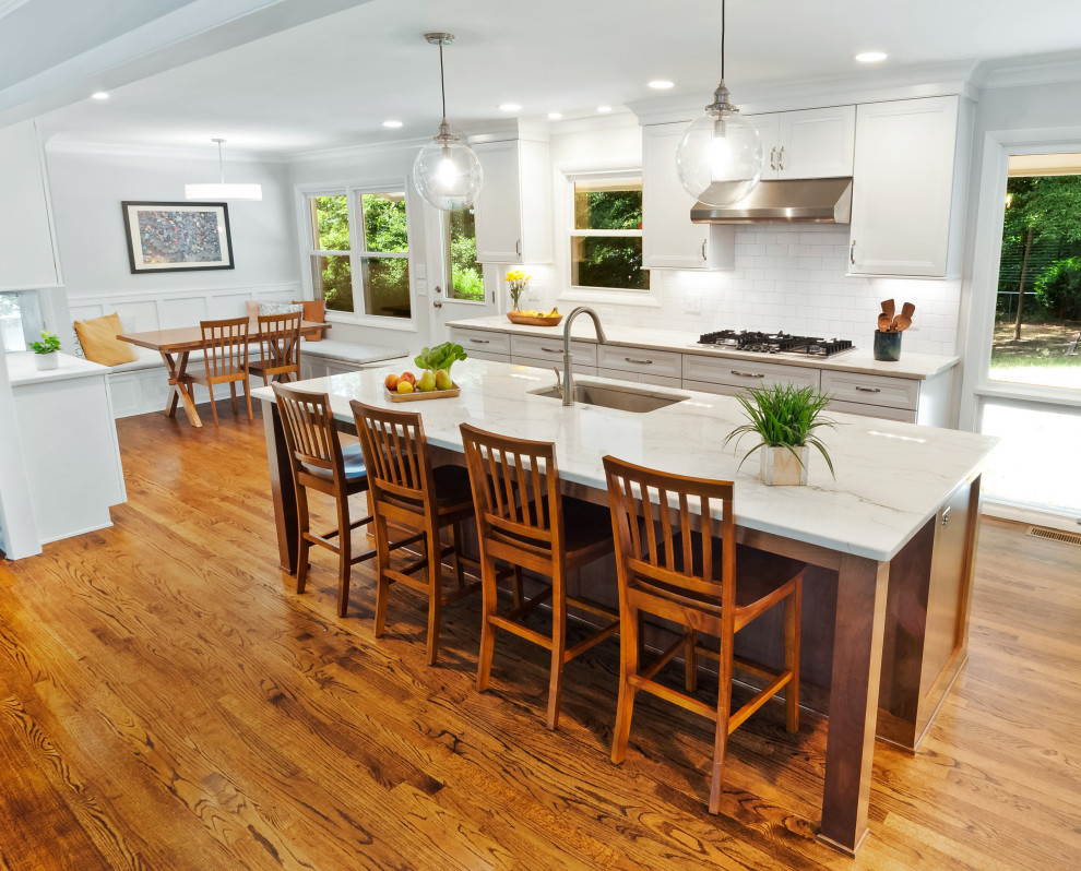 Example of a mid-sized transitional l-shaped medium tone wood floor and brown floor open concept kitchen design in Raleigh with a single-bowl sink, recessed-panel cabinets, white cabinets, quartzite countertops, white backsplash, porcelain backsplash, stainless steel appliances, an island and white countertops