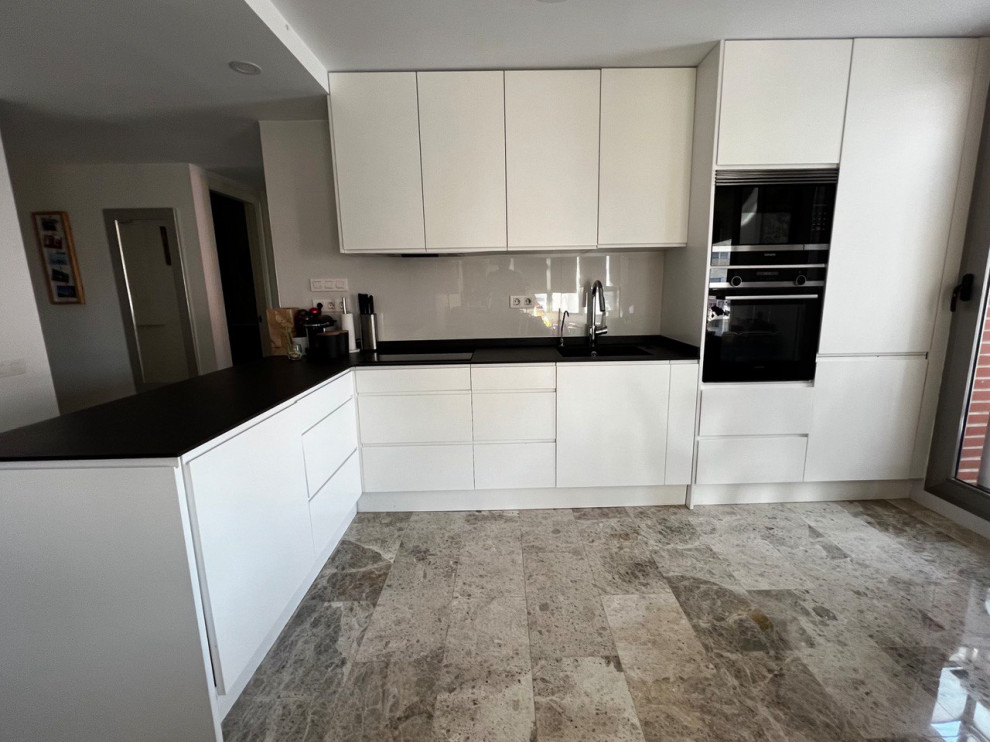This is an example of a small contemporary l-shaped kitchen/diner in Valencia with a submerged sink, flat-panel cabinets, tile countertops, white splashback, porcelain splashback, black appliances, marble flooring, grey floors and black worktops.