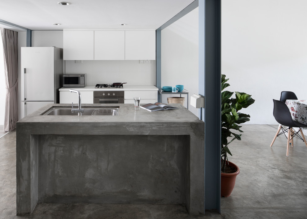 Inspiration for an industrial galley kitchen in Singapore with a drop-in sink, flat-panel cabinets, white cabinets, concrete benchtops, white splashback, white appliances, concrete floors, multiple islands, grey floor and grey benchtop.