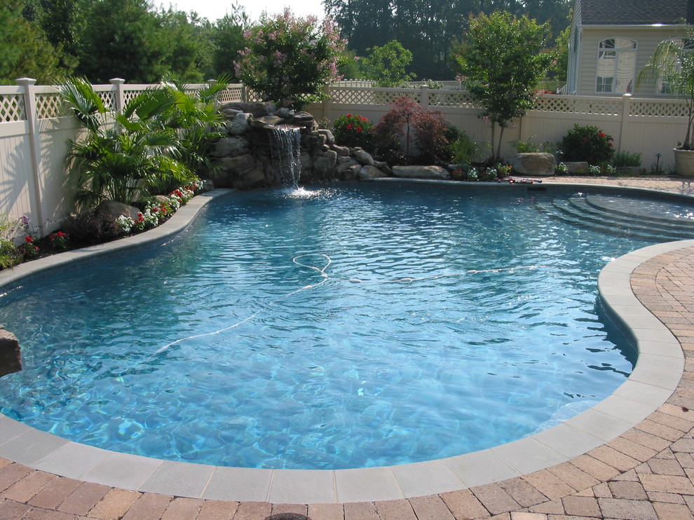 This is an example of a mid-sized traditional backyard kidney-shaped natural pool in Baltimore with a water feature and concrete pavers.